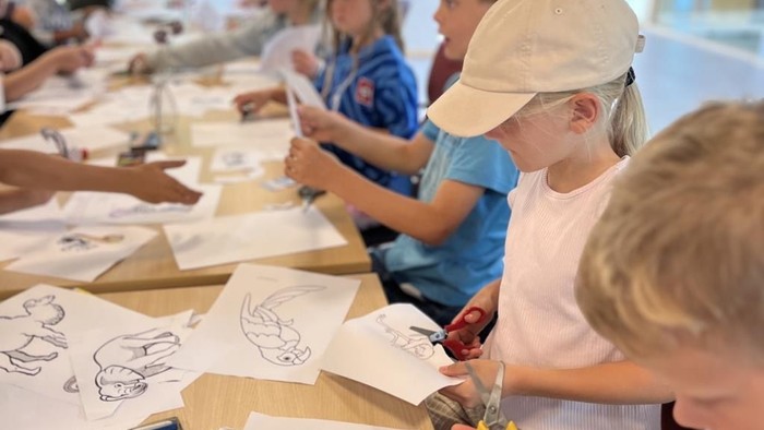 Børn sidder ved bord og laver tegninger i en lys og rummelig lokalitet.