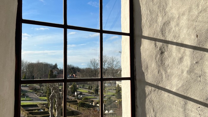 Et stort buet vindue med udsigt til en omhyggeligt anlagt have under en klar blå himmel.