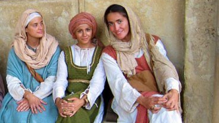 Drei Frauen in traditioneller Kleidung posieren vor einer Steinmauer