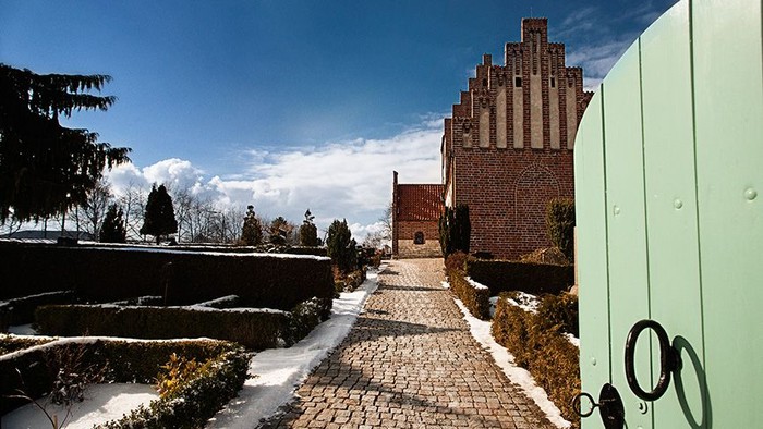 En stenvej leder op til en middelalderlig borg med tårn, omgivet af sne og træer