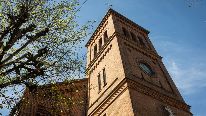 Tårn på kirke med klokke og træ med blomster.