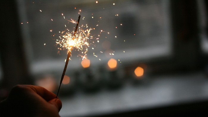 En hånd holder en lyse sparkler i mørke omgivelser