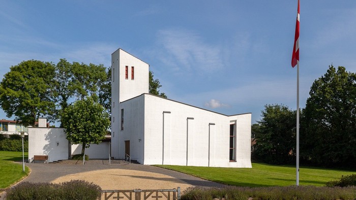 Et hvidt moderne kirkebygning med en flagstang med rødt flag foran