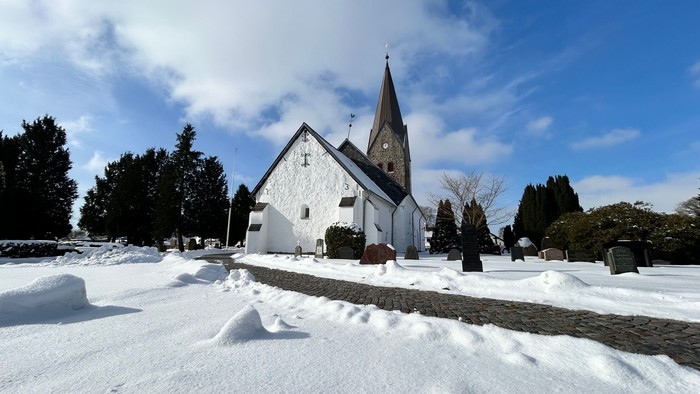 En fredfyldt snedækket kirke med et højt spir står midt i en stille, vinterlig kirkegård.