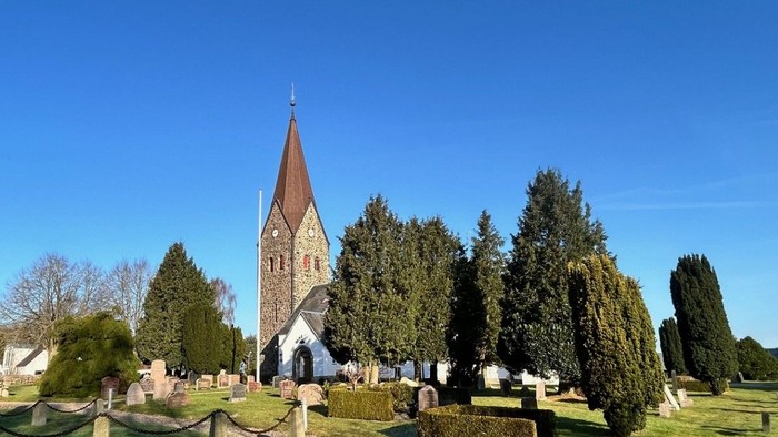 Solbeskinnet kirkegård med historisk kirketårn og spredte gravsten på en klar dag.