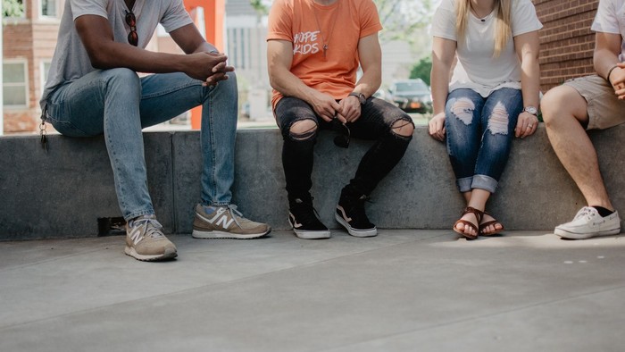 Drei Freunde sitzen auf einer Betonmauer und unterhalten sich.