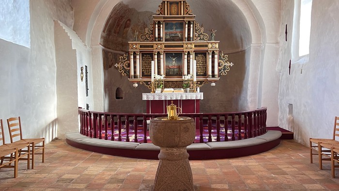 Kirken har høje buegange og en altertavle med guld.