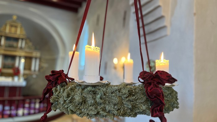 En hængende kranse med lys og røde bænker i kirke.