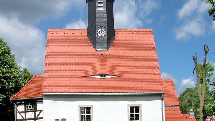 Kleine weiße Kirche mit rotem Dach und schwarzem Turm.