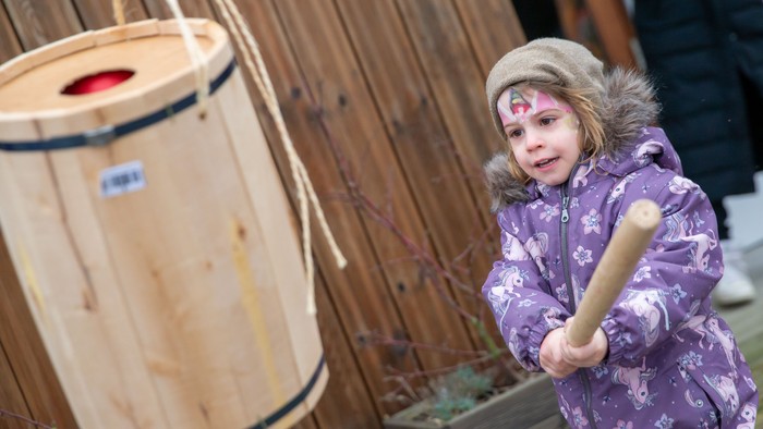 Et lille barn i fjer, der slår på en trætromme med en stav.