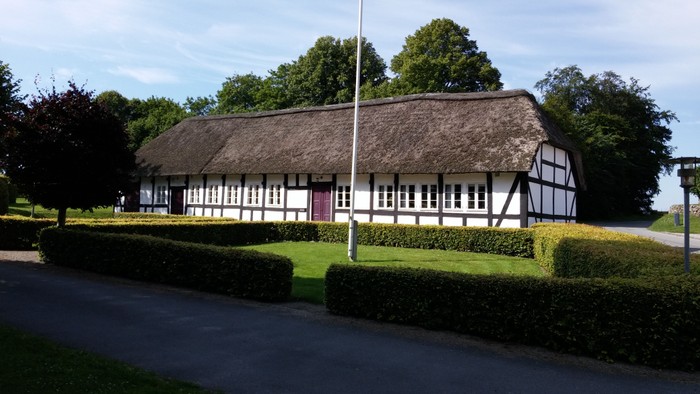 En hvid og sort staldet hus med trætag og omgivet af buske og træer