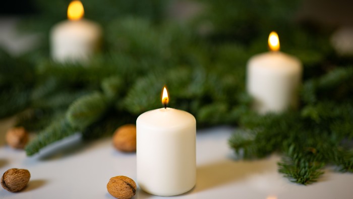 Drei brennende Kerzen, umgeben von Grünpflanzen und Nüssen.