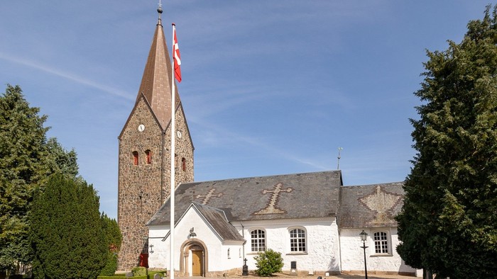 En hvid kirke med tårn og flag på en klar dag