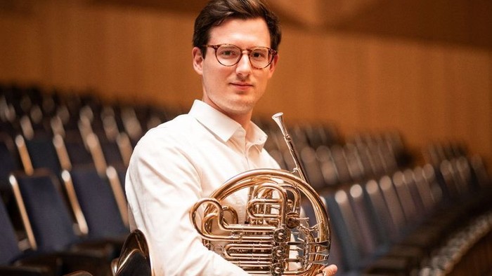 Mann, der ein Waldhorn in einem Auditorium hält.