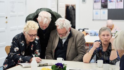 En gruppe ældre personer sidder om bordet og diskuterer.