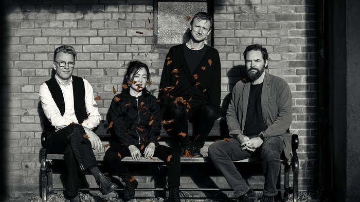 Fire personer, der sidder på en bænk op ad en murstensvæg.