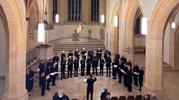 Ein Chor tritt in einer prächtigen, historischen Kirche mit aufwendiger Architektur auf, während das Publikum unten sitzt.