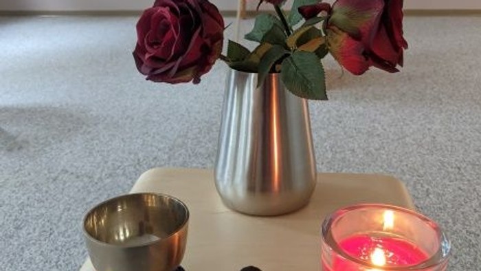 Ein Blumenstrauß in einer Vase, eine brennende Kerze und ein kleines Schälchen auf einem Holztisch