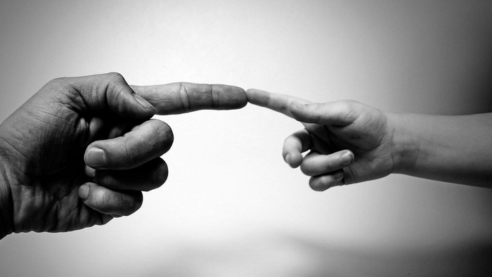 To hands træffer hinanden med fingrene.