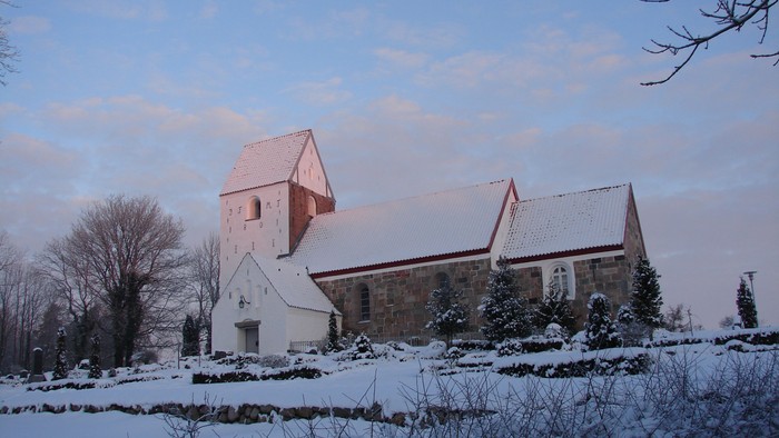 En snede kirke med tårn og træer i sne.