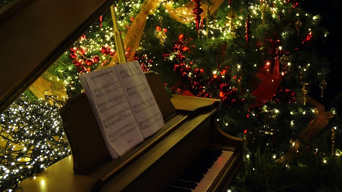 En juletree med lys og pynt til venstre for et piano med noter.