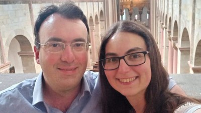 Zwei Personen, die in einem historischen architektonischen Ambiente mit Bögen und Säulen für ein Selfie lächeln.