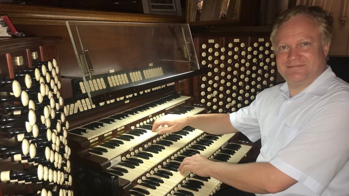 Ein Mann spielt eine komplexe Pfeifenorgel mit mehreren Manualen und Registern.