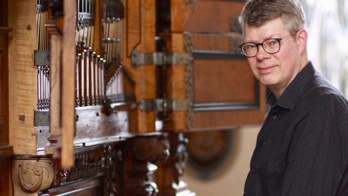 En mand med briller står ved siden af et indviklet designet orgelpult.