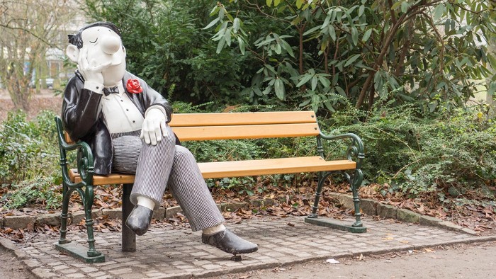 Loriot-Figur mit Knollnase sitzt auf einer Parkbank