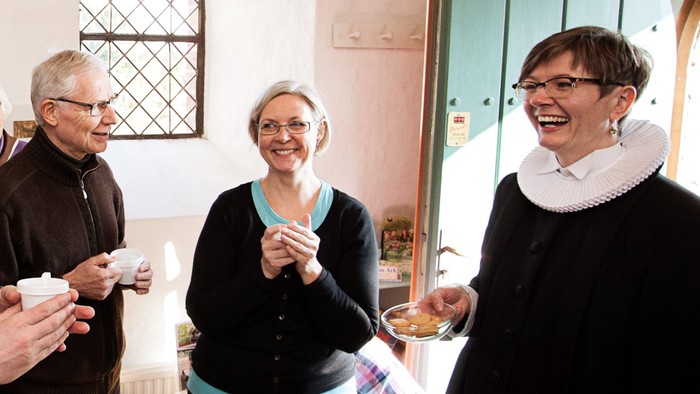 En gruppe af voksne står sammen og holder tærtekniver, tilsyneladende i festlig stille.