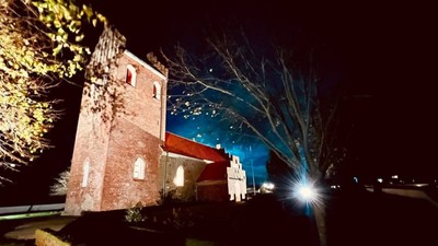 En mørk nattscene med en belyset murstenskirke og et træ.