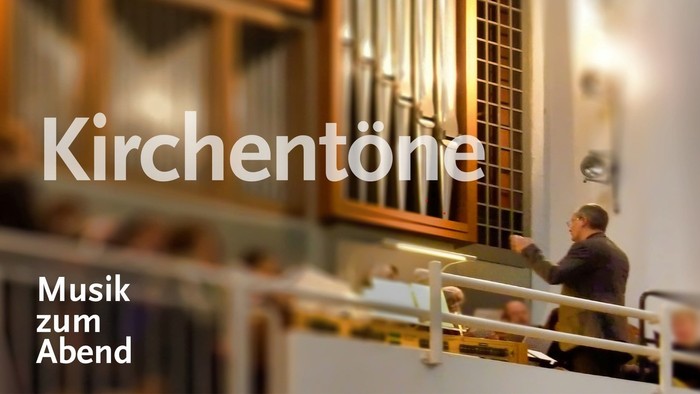 Ein Mann spielt Kirchenorgel, umgeben von Kirchenfenstern und Kirchenbänken