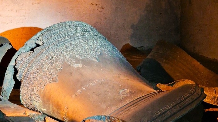 Alte, verwitterte Statue einer liegenden Figur in einer düster beleuchteten, rustikalen Umgebung.