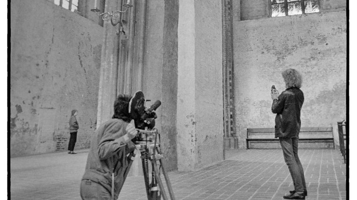 Fotograf, der in einer alten Kathedrale mit der Kamera kniet und architektonische Details festhält, während eine andere Person zuschaut.
