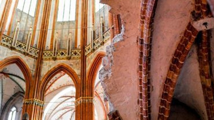 Gotischer Kathedraleninnenraum mit hohen Säulen, Bögen und einem markanten Kruzifix unter Buntglasfenstern.