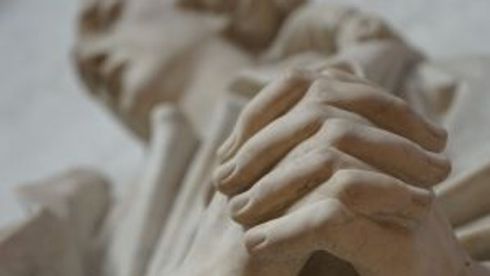 Die Statue zeigt eine Person in nachdenklicher Haltung.