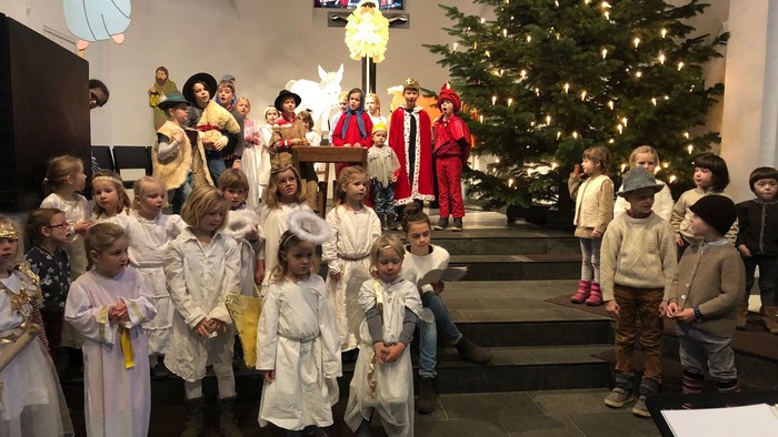 Kinder in weißen Kleidern singen vor Weihnachtsbaum