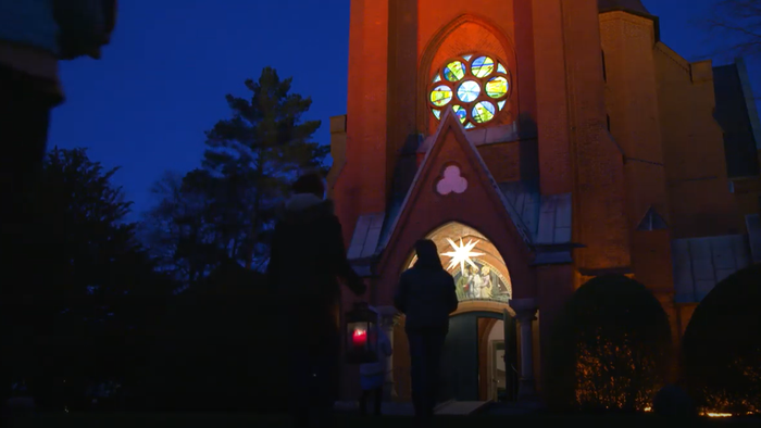 Kirchengebäude bei Dämmerung mit beleuchteten Fenstern und Bäumen davor