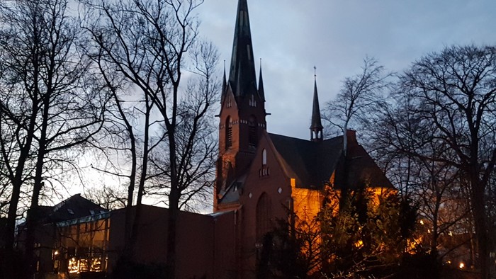 Gothische Kirche bei Dämmerung, umgeben von kahlen Bäumen