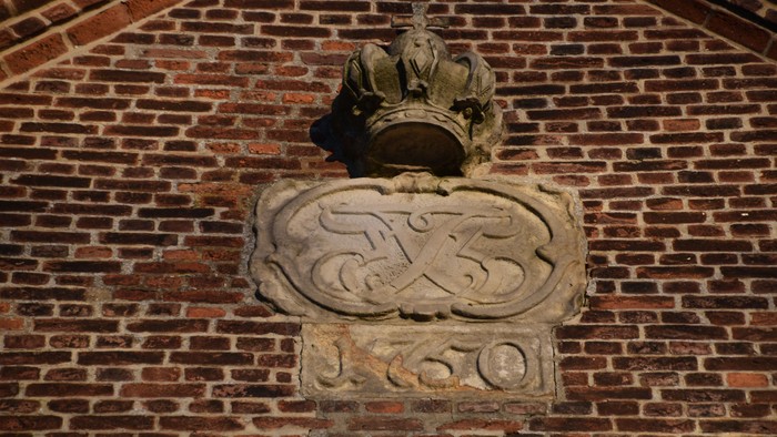 Zierstein-Wappen mit Krone und verschlungenen Buchstaben „J“ und „S“ über der Jahreszahl 1550 an einer Backsteinmauer.