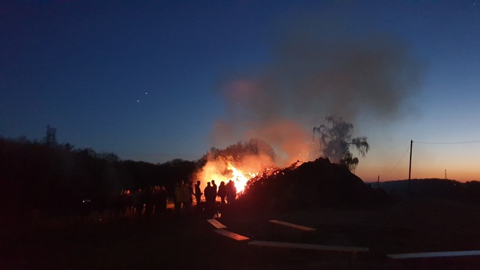 Nachtliche Szene mit brennender Müllhalde und Menschen.