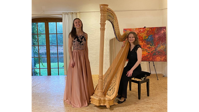 Sophia Desirée Bauer in langem pastelfarbenem Kleid links, Harfe, Giedrė Šiaulytė in schwarzem Hosenanzug rechts und im Hintergrund ein Fenster und ein Bild
