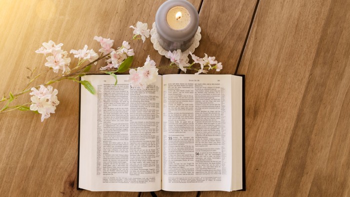 Offenes Buch mit Kerze und Blumen auf Holzboden