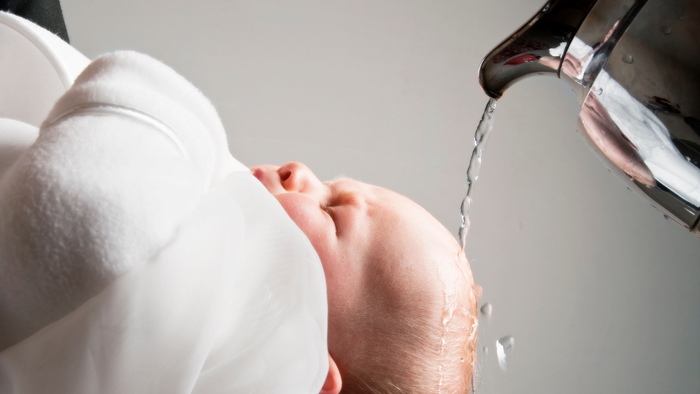 Ein Baby wird mit Wasser aus einer Kanne über den Kopf gewaschen.