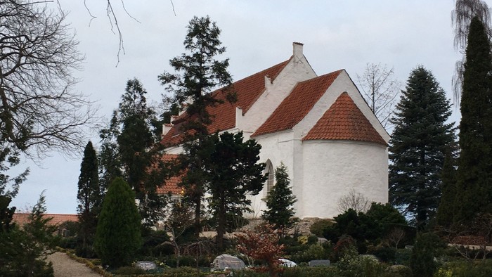 Hvid kirke med rødt tag og omgivet af træer og buske