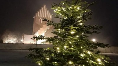 En juletree med lys i forgrunden og et belyset tårn i baggrunden