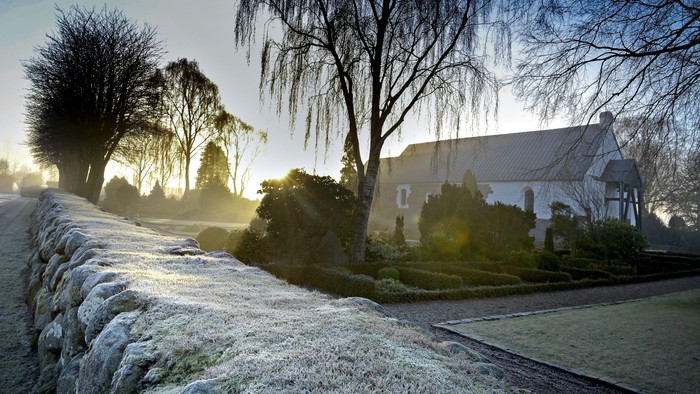 En frosten og sollysede haveskov med en stenmur og et hvidt hus i baggrunden