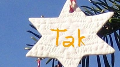 En hvid stjerneformet pynt med navnet "Tak" hænger i et træ.