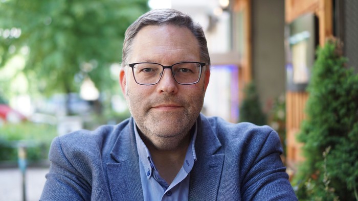 Mann mit Brille sitzt draußen vor einem Gebäude.