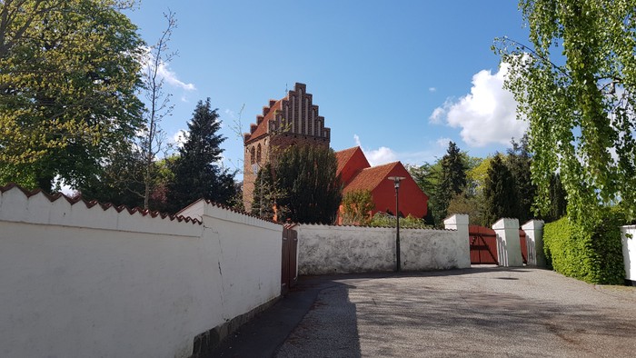 En hvid mur med en indgang til en trækirke med røde tag.